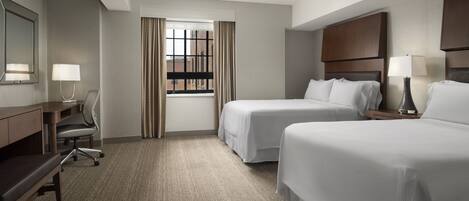 A hotel room with two beds, a desk, a chair, a lamp, and a window with curtains.