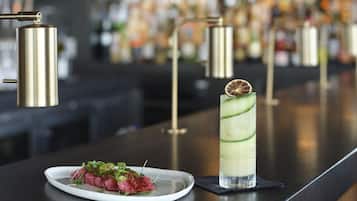 Une assiette blanche remplie de nourriture est posée sur un comptoir de bar, à côté d’un grand verre contenant une boisson verte.