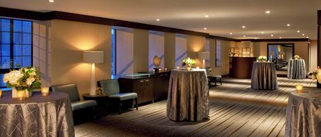 A hotel lobby with round tables, chairs, and a reception desk.