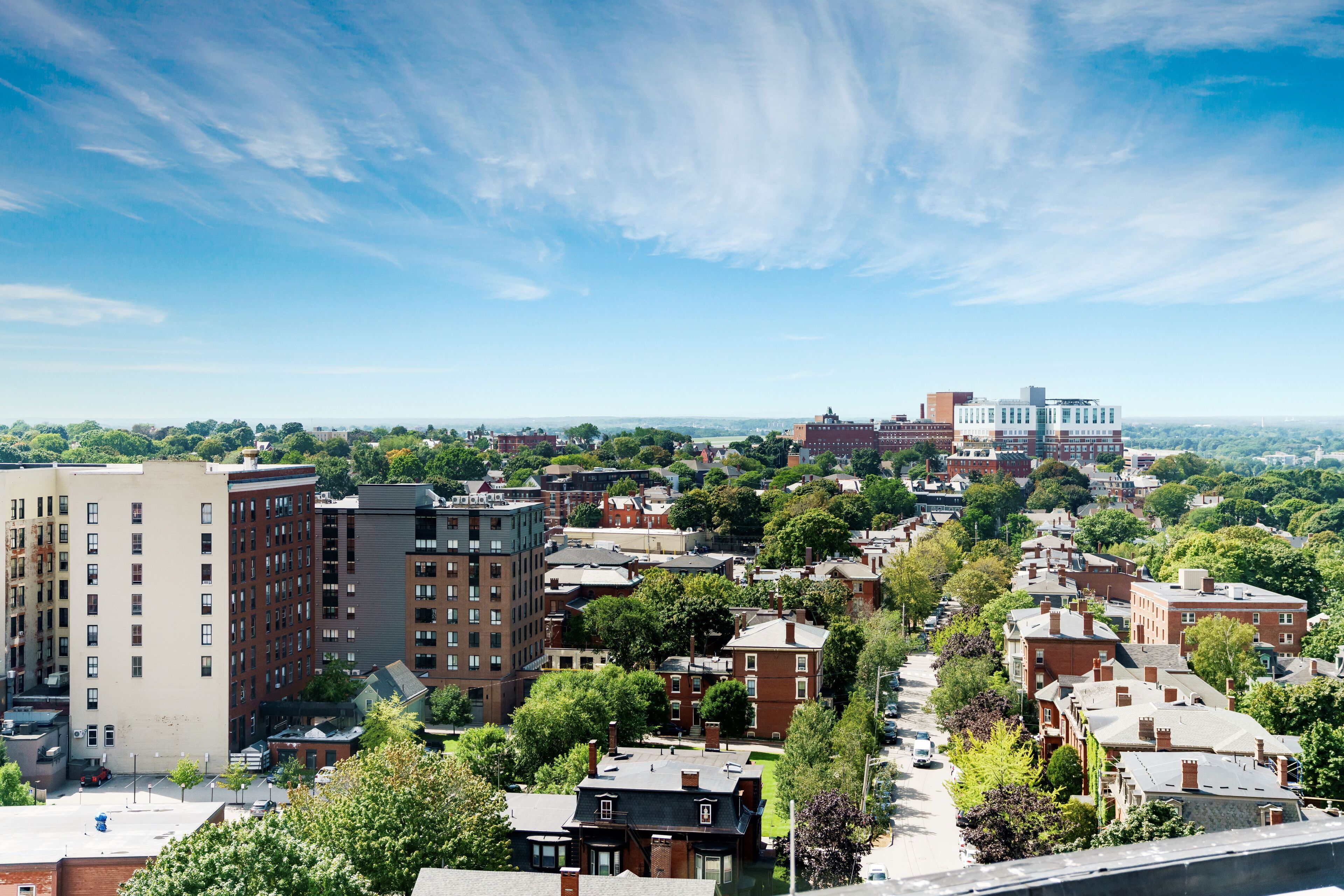 A cityscape with a mix of residential and commercial buildings, a clear sky, and a distant view of a larger city.
