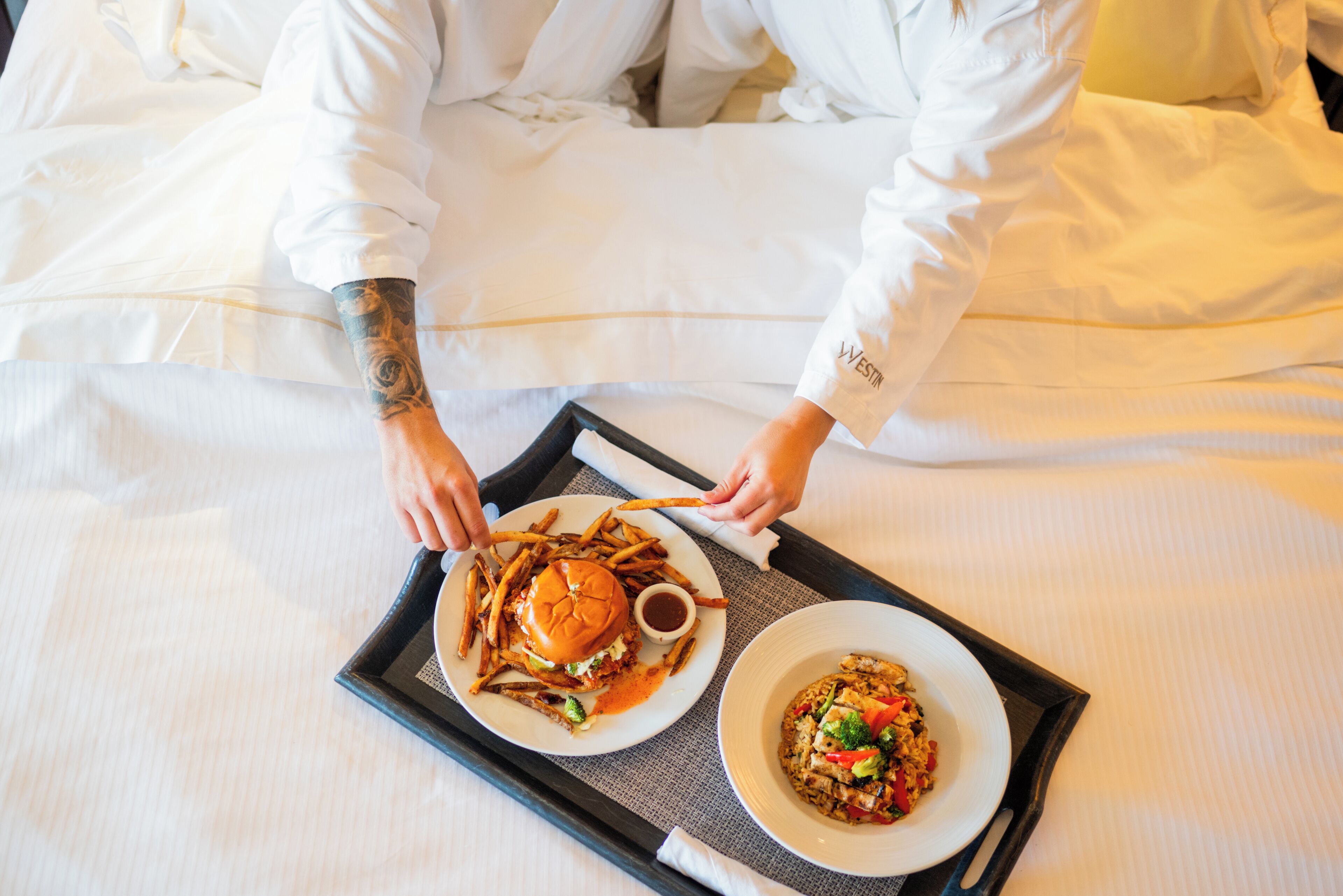 A person serving a burger and a plate of food on a tray.