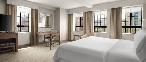 A hotel room with a large bed, a desk with a chair, a television, and a window with curtains.