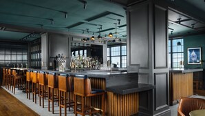 Una zona de bar con una barra larga, varios taburetes y una amplia variedad de botellas y vasos.