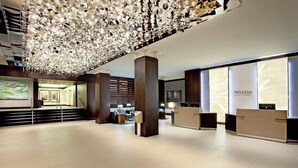 Un moderno vestíbulo de hotel con una gran lámpara de araña, mostrador de recepción y una escalera que conduce a otras áreas.