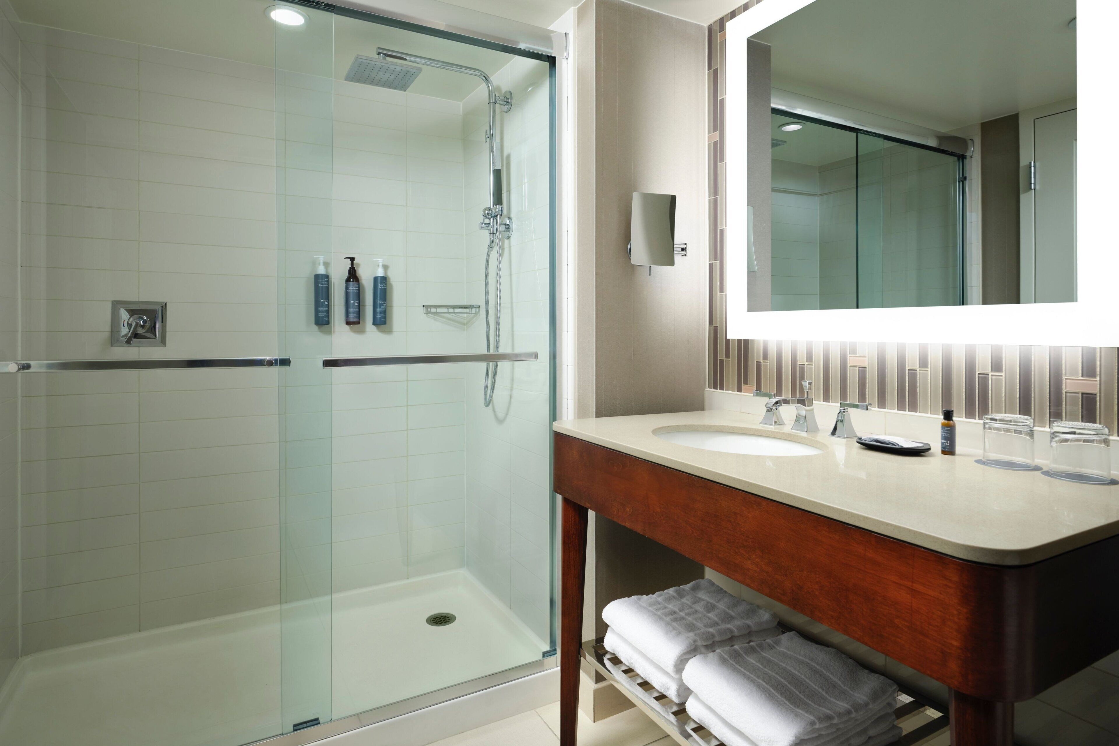 A modern bathroom with a glass-enclosed shower, a large mirror, and a vanity with a sink and towel rack.