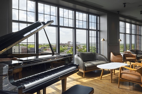 A grand piano in a spacious room with large windows, leather chairs, and a small table.
