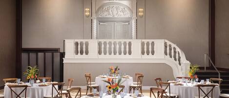 Une salle de banquet avec des tables rondes, des nappes blanches et des chaises en bois.