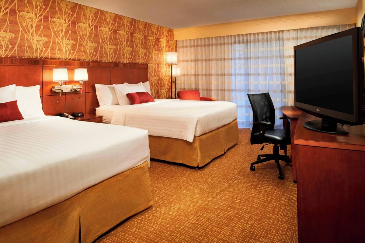 Een hotelkamer met twee bedden, een bureau, een televisie en een raam met gordijnen.