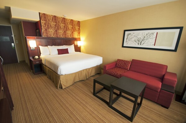 A hotel room with a large bed, a red sofa, a small table, and a framed picture on the wall.