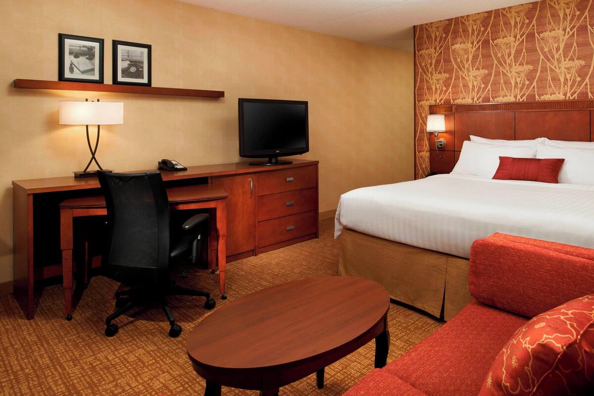 Een hotelkamer met een bed, een bureau met stoel, een televisie, een lamp en een klein tafeltje.