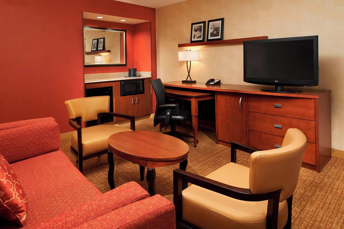 Een hotelkamer met een bank, twee stoelen, een bureau met een televisie, een lamp en een magnetron.