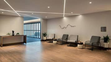 A modern reception area with a reception desk, four grey armchairs, and potted plants.