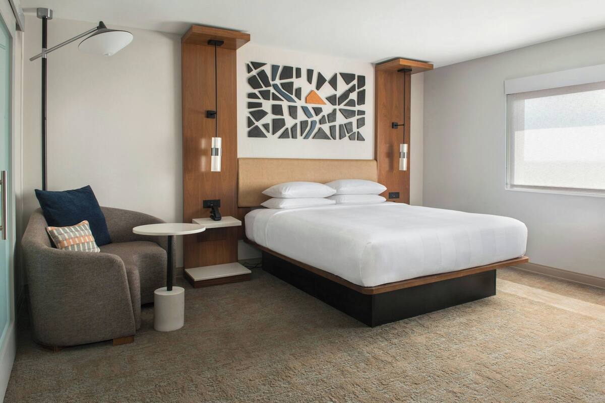 Un dormitorio moderno con una cama grande, una mesita de noche pequeña, una silla y una lámpara de pie.