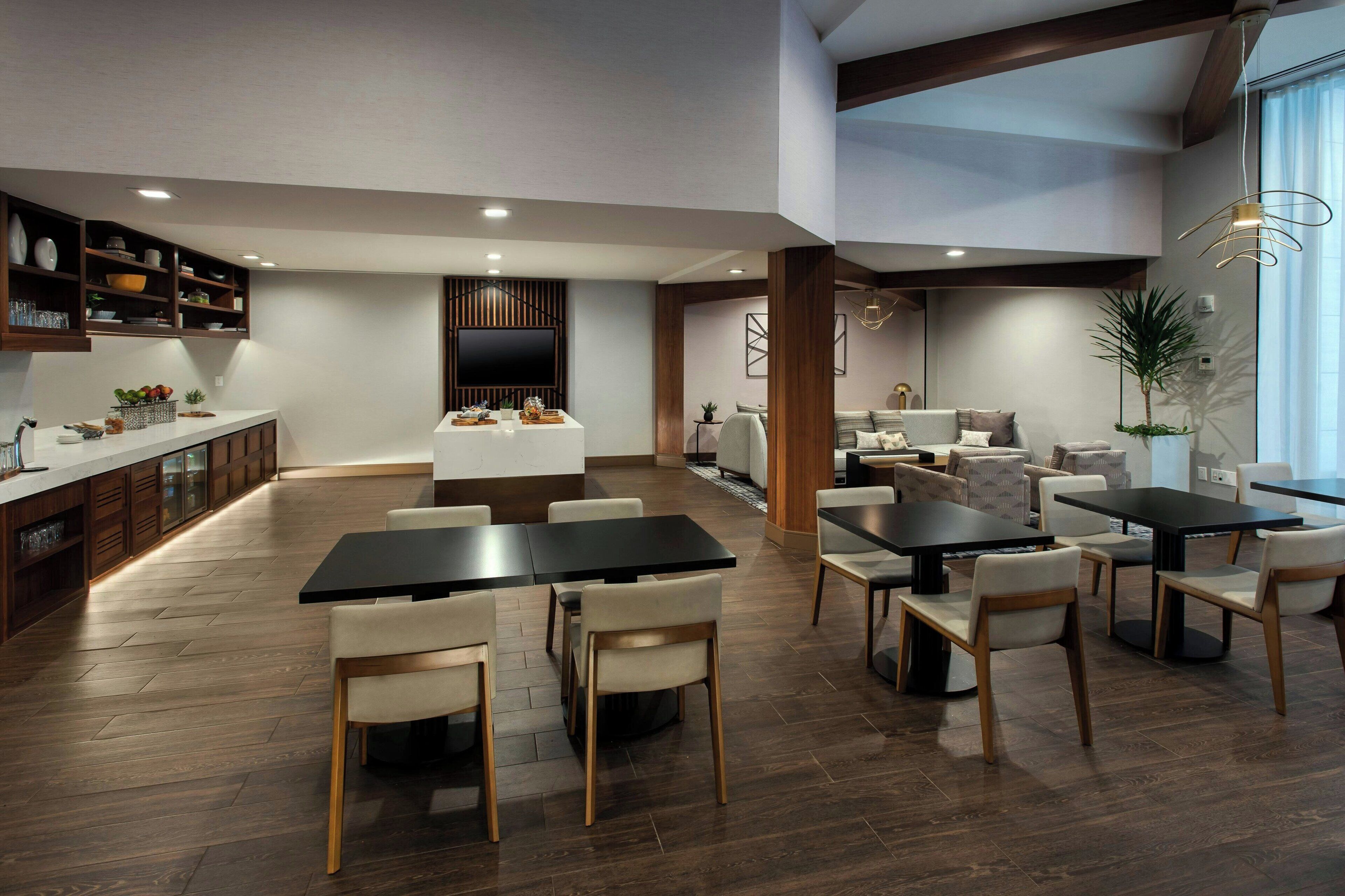 A modern kitchen with wooden cabinets, a central island, and a dining area with a large table and chairs.