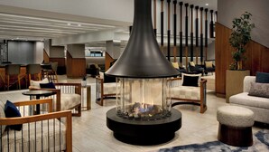 A modern lounge area with a central fire feature, comfortable seating, and a staircase in the background. - Marriott Springfield Downtown (Springfield)