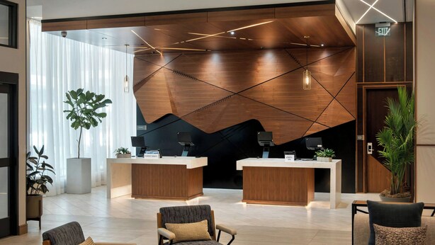 A modern reception area with two reception desks, a seating area with armchairs and a sofa, and a large plant. - Marriott Springfield Downtown (Springfield)