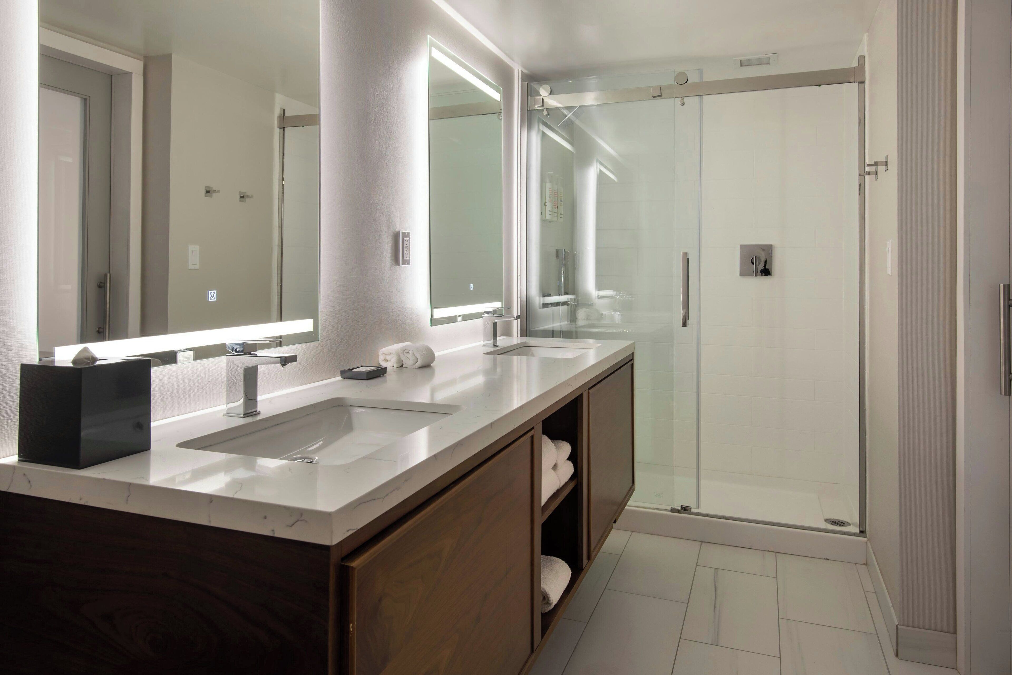 A modern bathroom with a double sink vanity, a large mirror, and a glass-enclosed shower.
