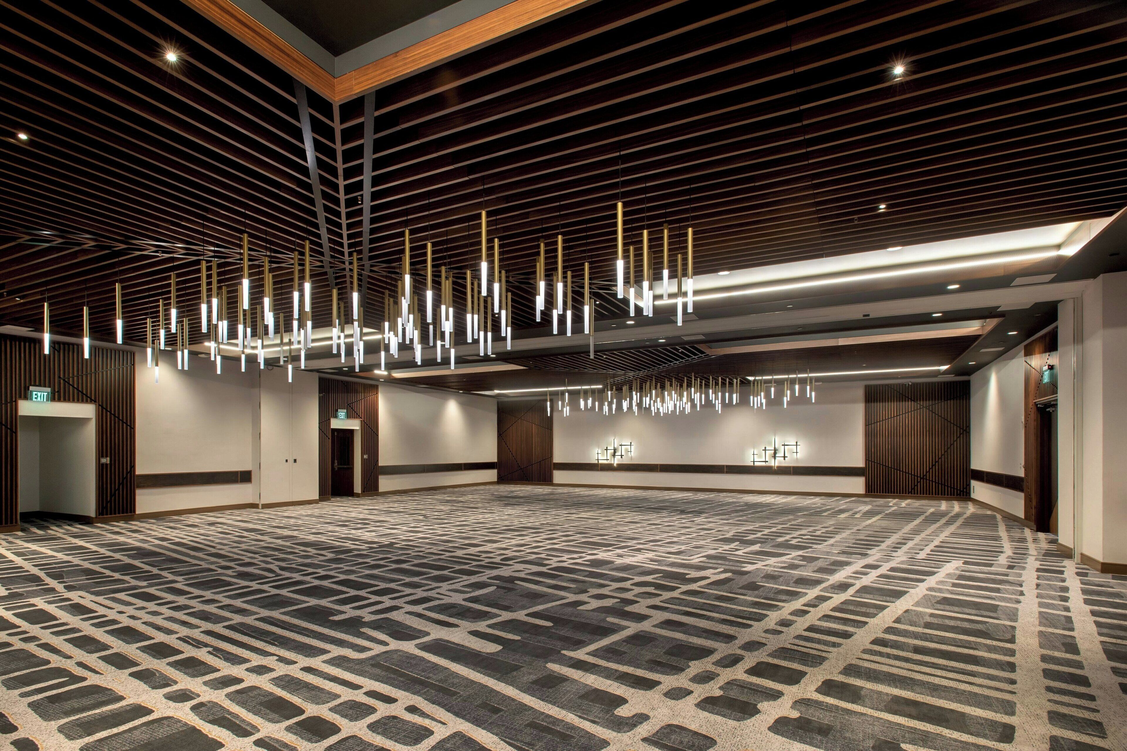 Uma sala de conferências ampla com carpete estampado, painéis de madeira nas paredes e iluminação pendente moderna.