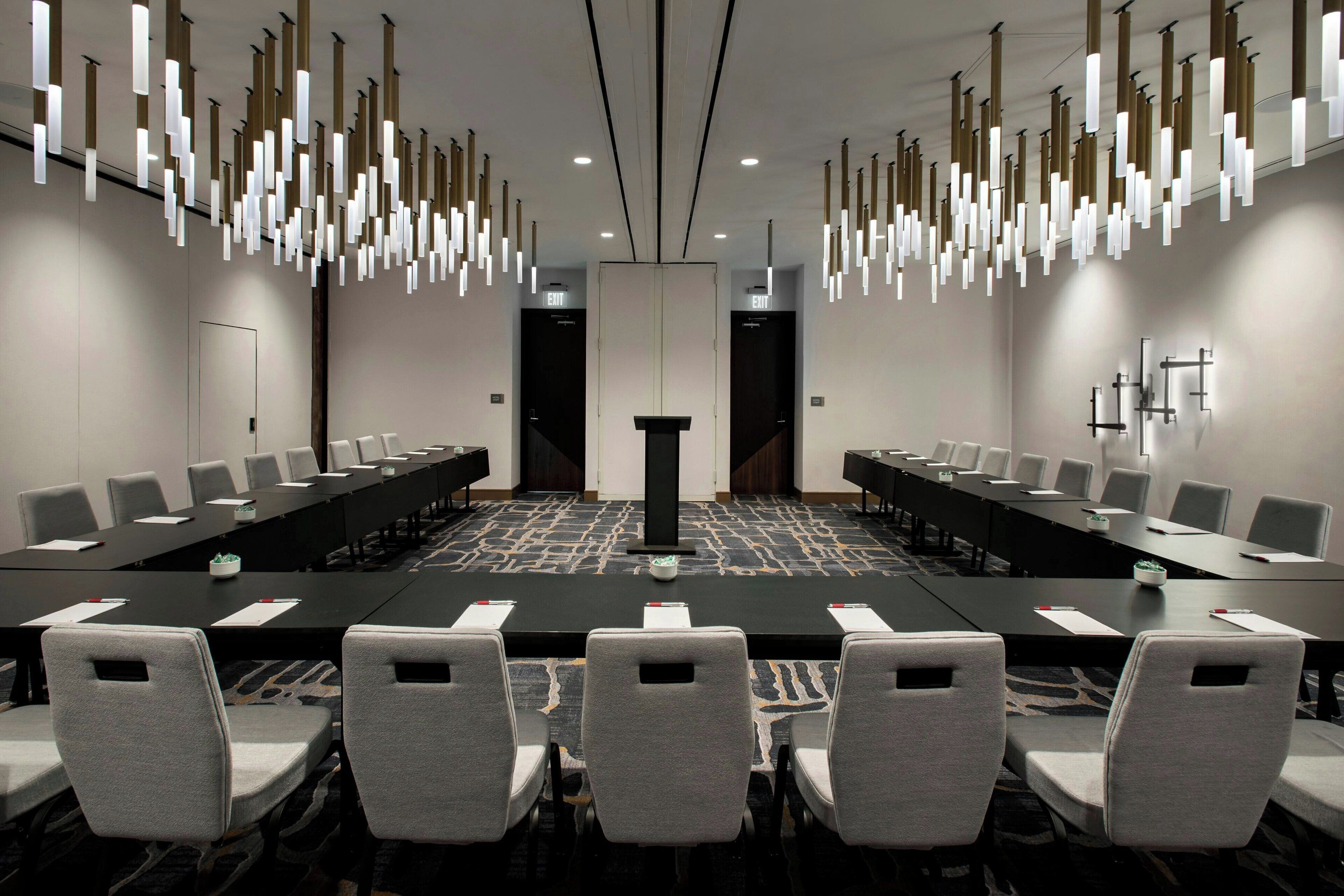 Un salón de conferencias con una larga mesa, múltiples sillas e iluminación colgante moderna.