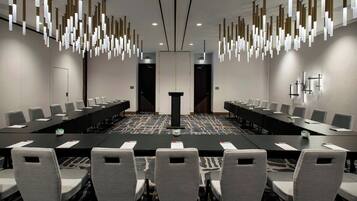 Un salón de conferencias con una larga mesa, múltiples sillas e iluminación colgante moderna.