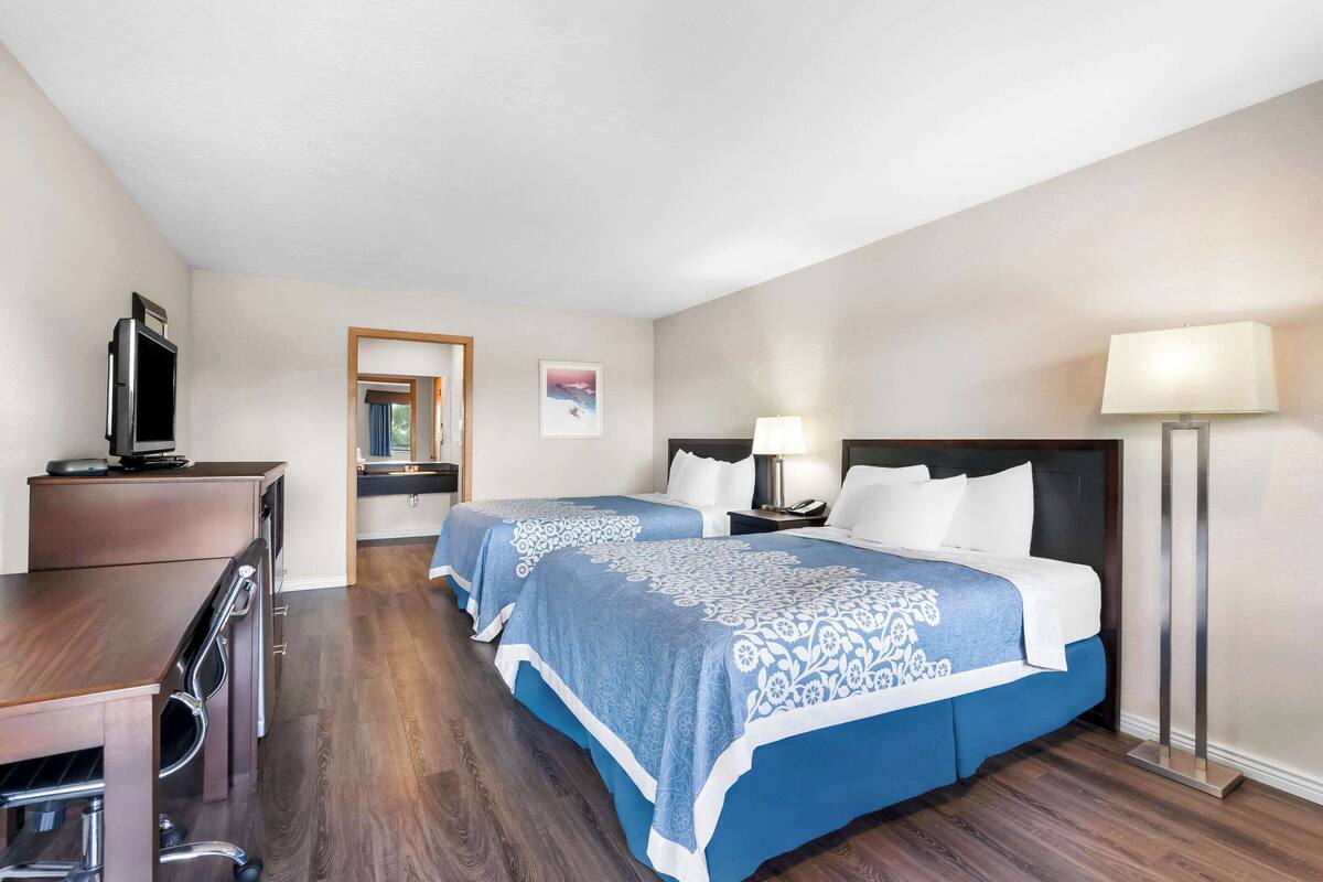 A hotel room with two beds, a desk, a TV, and a lamp.