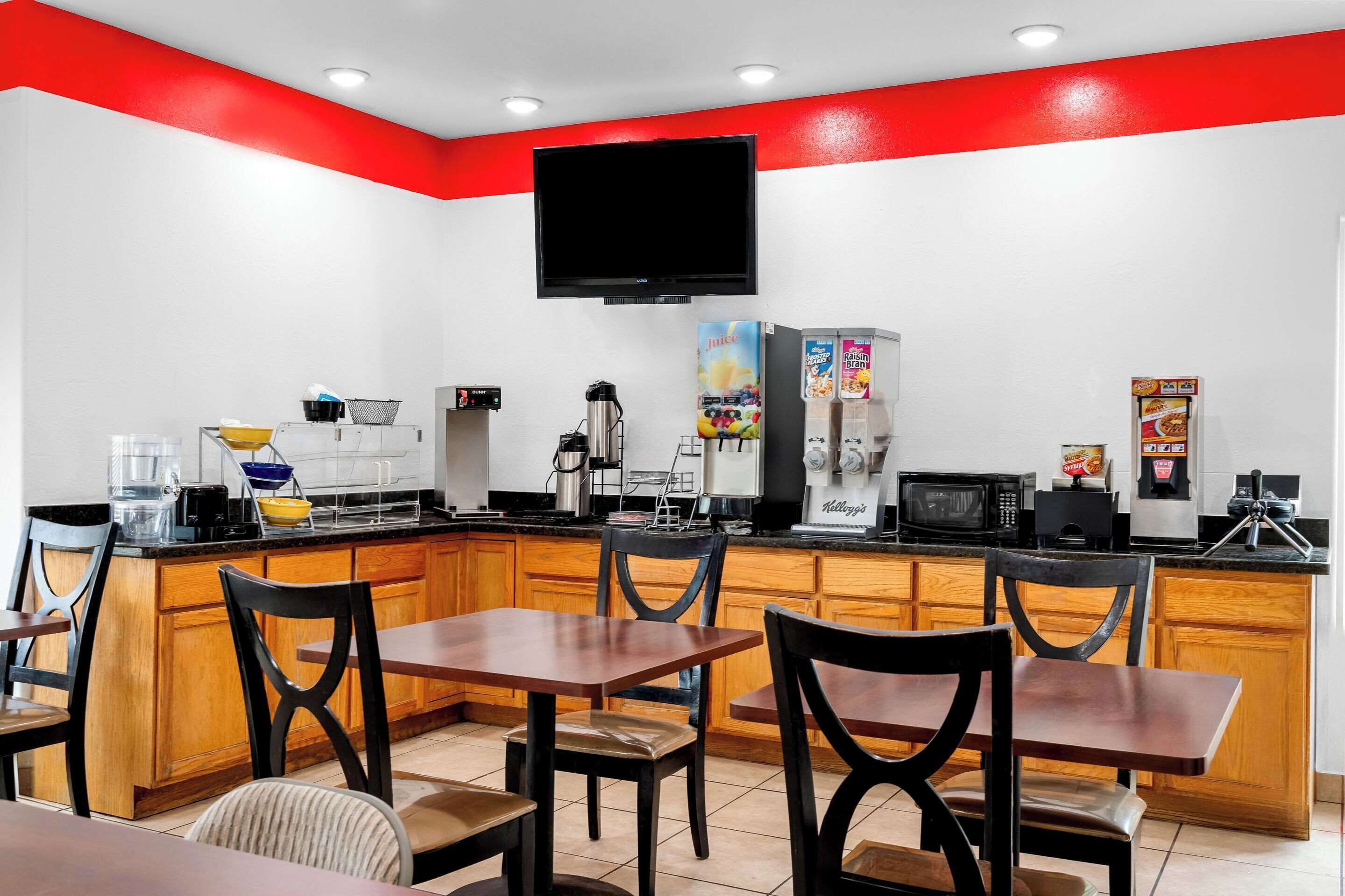 A modern kitchen with wooden cabinets, a black countertop, and a red accent wall.