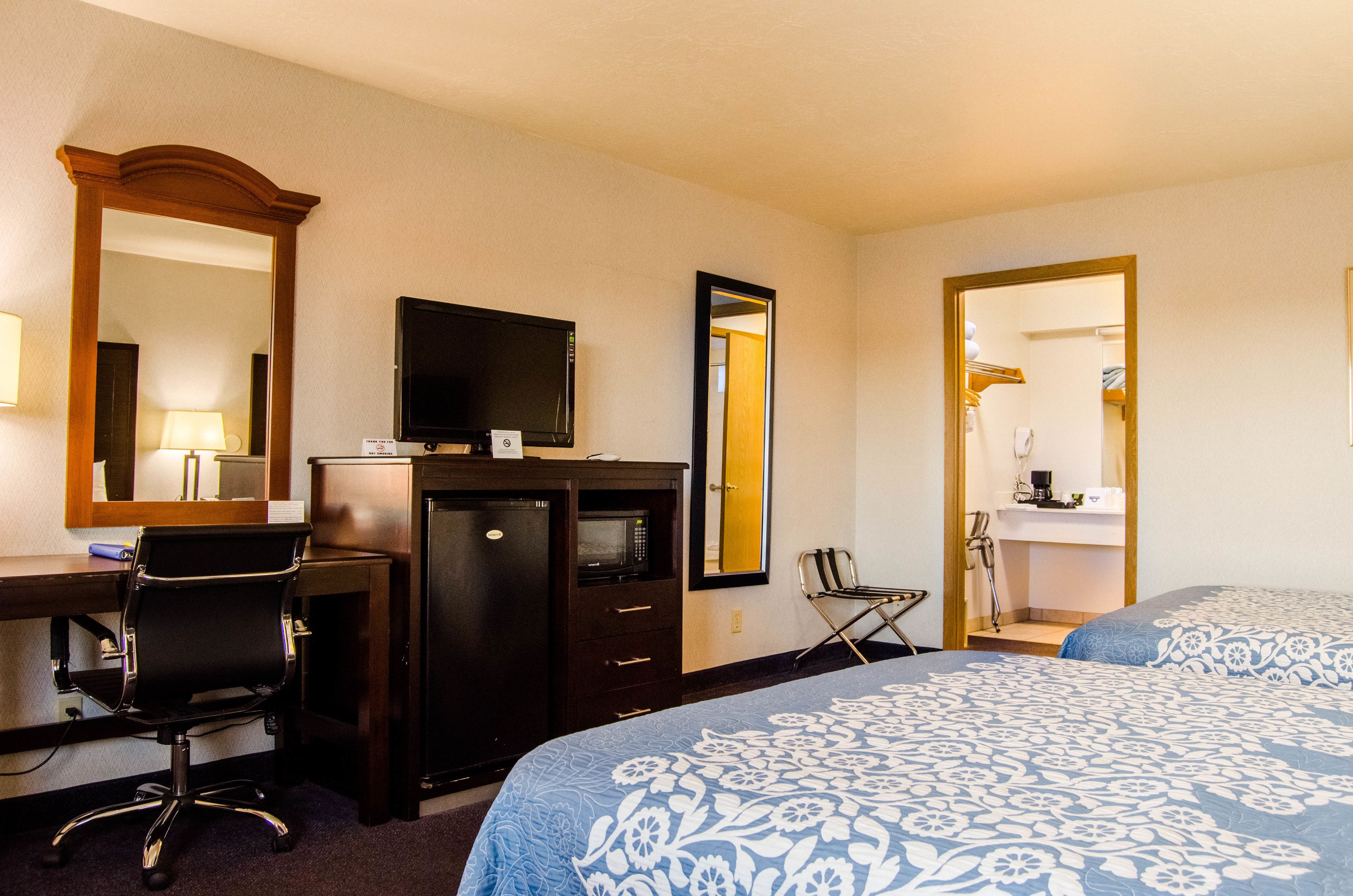 A hotel room with a desk, chair, television, and two beds with patterned bedding.