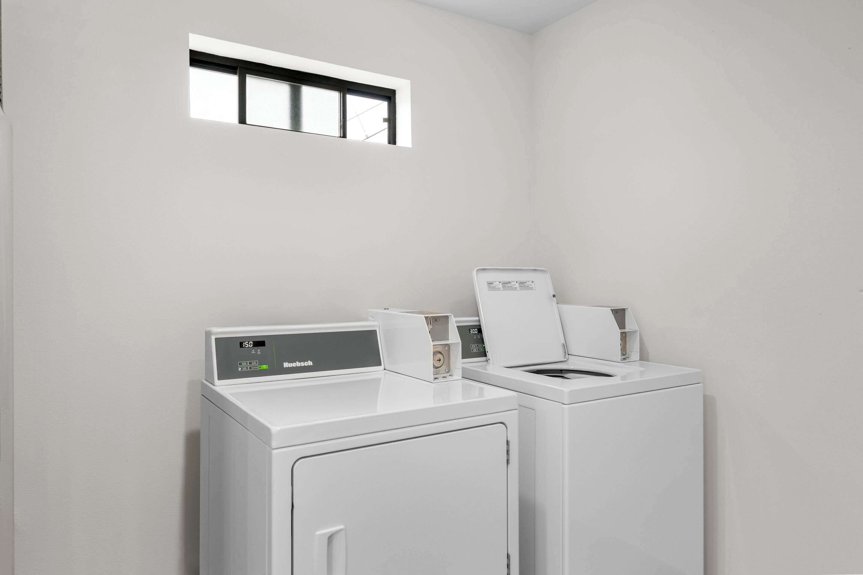 Une buanderie équipée de deux machines à laver blanches et d’une petite fenêtre située au-dessus.