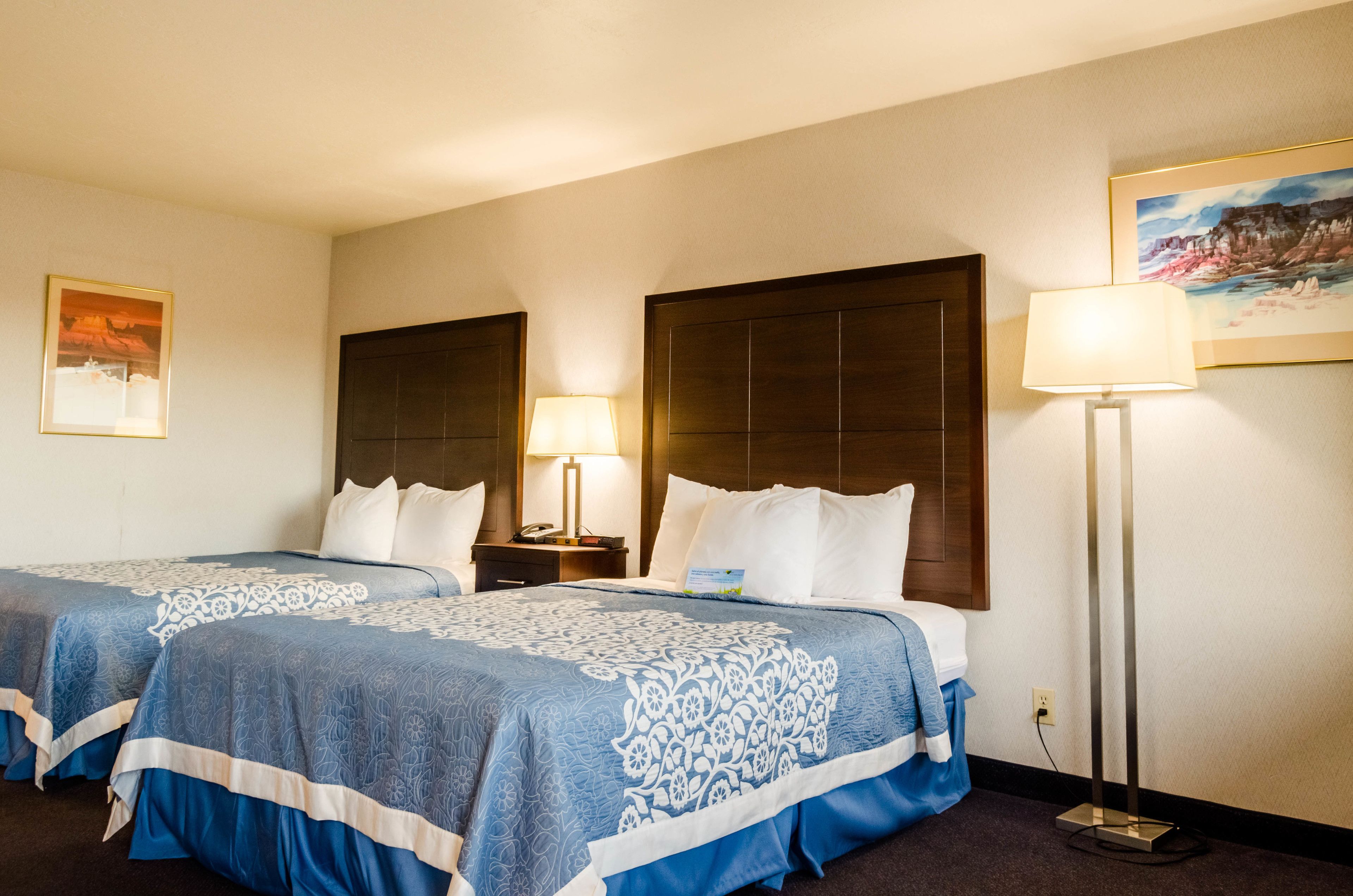 A hotel room with two beds, a nightstand, a lamp, and a painting on the wall.