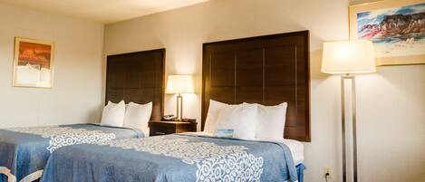 A hotel room with two beds, a nightstand, a lamp, and a painting on the wall.