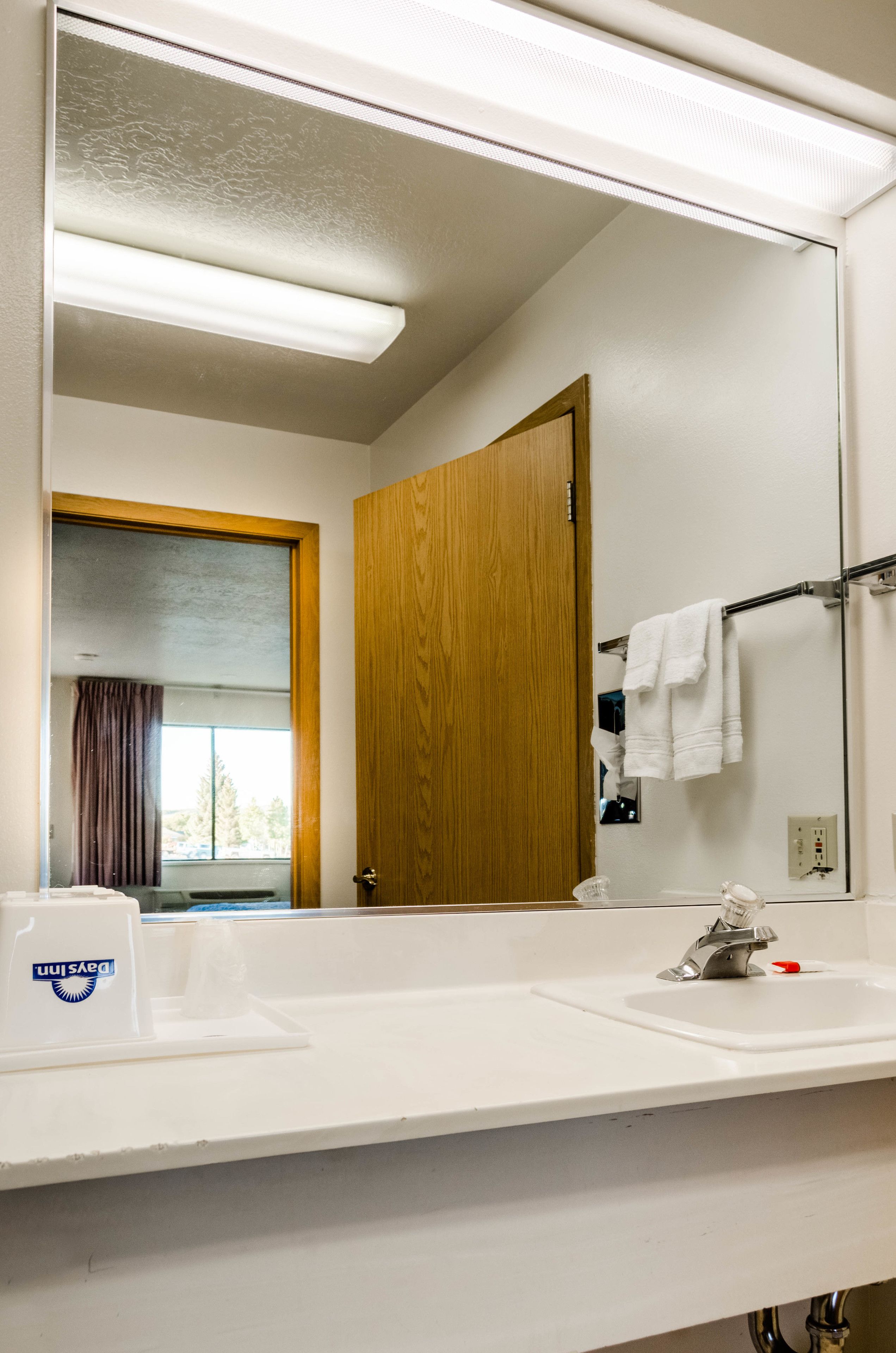 A bathroom with a large mirror, two sinks, a towel rack, and a door leading to another room.