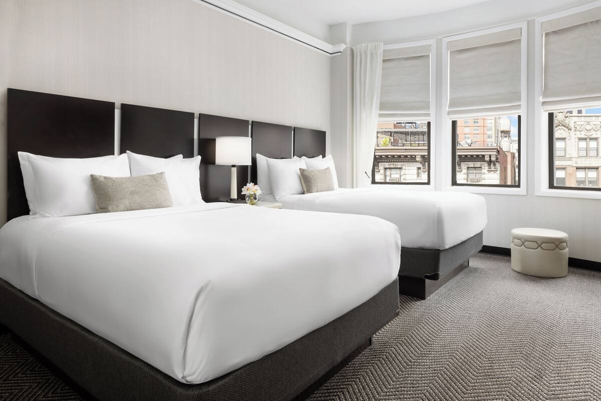 A hotel room with two beds, a large window, and a view of the city.