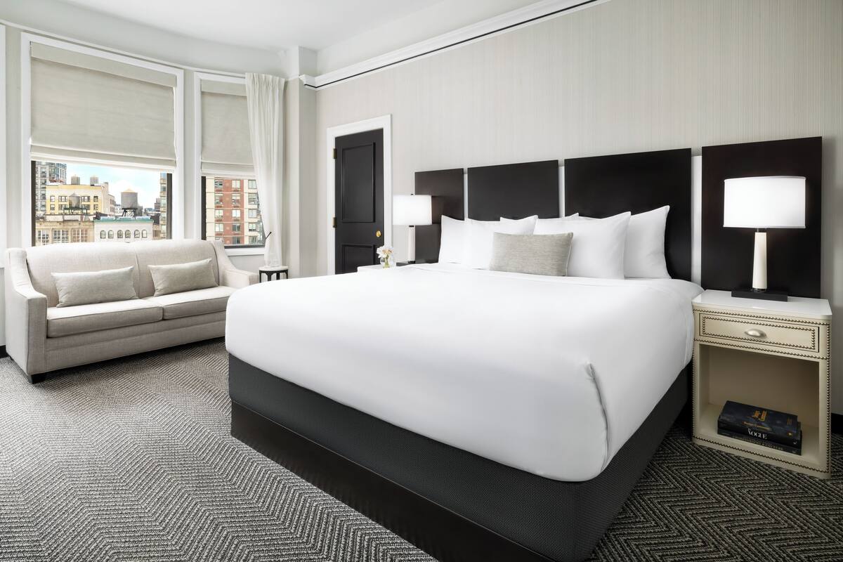 A modern hotel room with a large bed, a sofa, and a nightstand with a lamp.