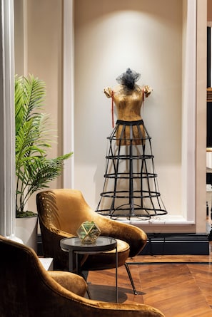 A room with a mannequin in a dress, a golden armchair, a small table with a plant, and a tall black metal sculpture. - The Gregorian New York City (New York)
