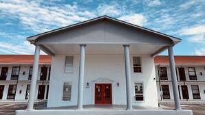 Un edificio blanco con puerta roja y columnas, con el número 3410, bajo un cielo despejado.