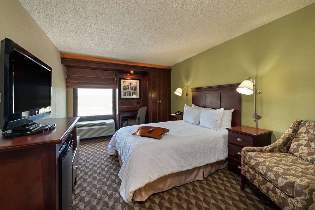 A hotel room with a large bed, a desk with a flat-screen TV, a chair, and a sofa.