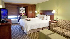 A hotel room with a bed, a television, a desk, a chair, a sofa, and a patterned floor. - Hampton Inn Baton Rouge - I-10 & College Dr. (Baton Rouge)