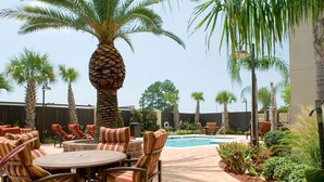 An outdoor patio with a pool, surrounded by palm trees and red flowers. - Hampton Inn Baton Rouge - I-10 & College Dr. (Baton Rouge)