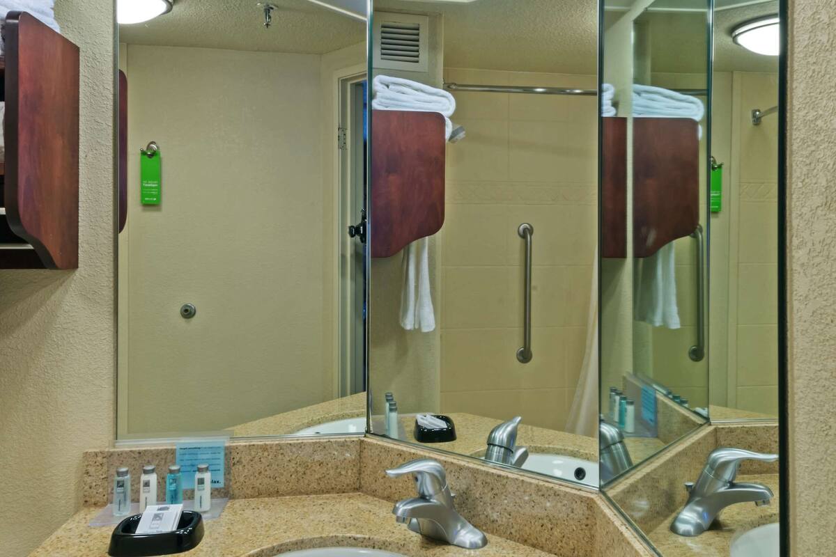 A bathroom with a granite countertop, two sinks, a large mirror, and a shower area.