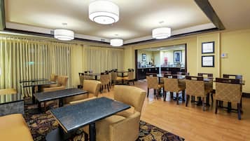 A hotel lobby with multiple seating areas, including tables and chairs, and a reception desk in the background.