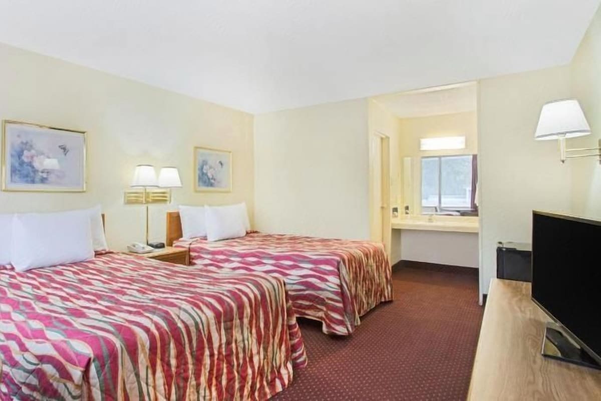 A hotel room with two beds, a desk, a television, and a bathroom visible through an open door.