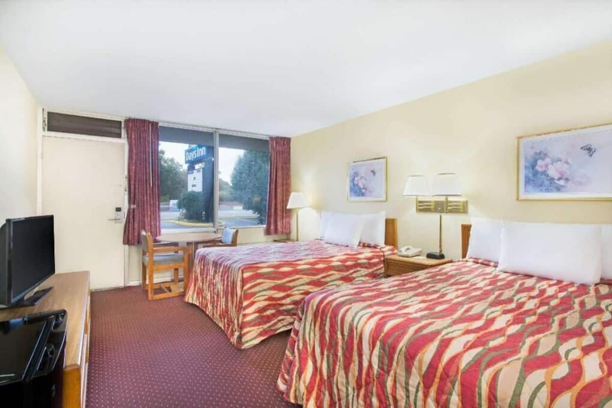 A hotel room with two beds, a television, a desk, and a window with curtains.