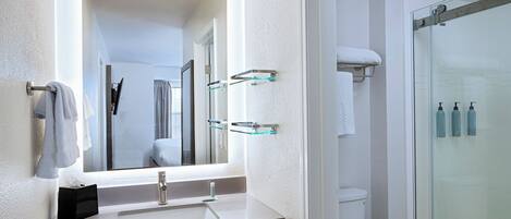 A bathroom with a sink, mirror, towel rack, and glass shower enclosure.