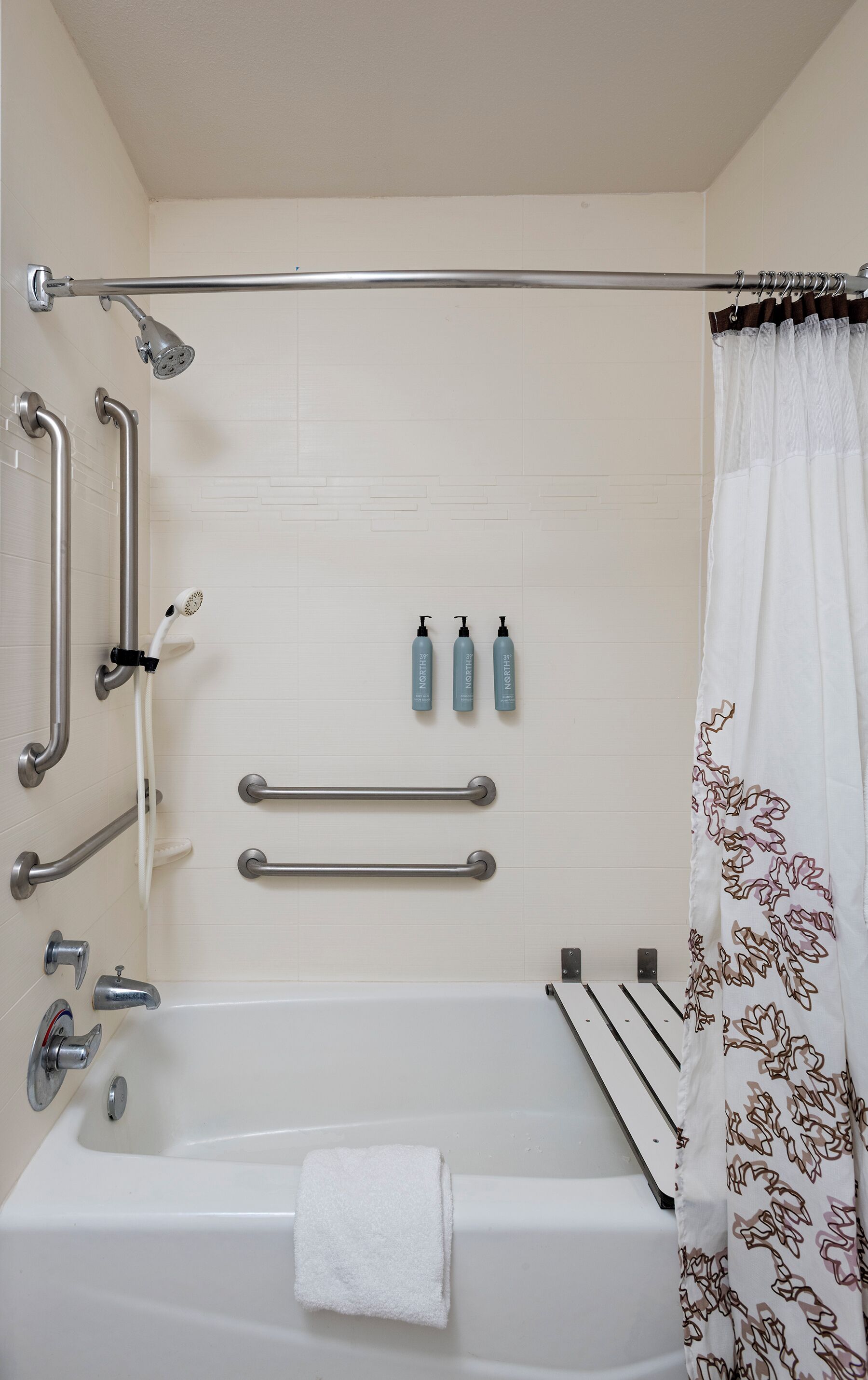 Une salle de bain équipée d’une baignoire, d’une douche, de barres d’appui et d’un porte-serviettes.