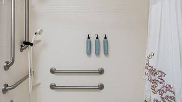 Une salle de bain équipée d’une baignoire, d’une douche, de barres d’appui et d’un porte-serviettes.