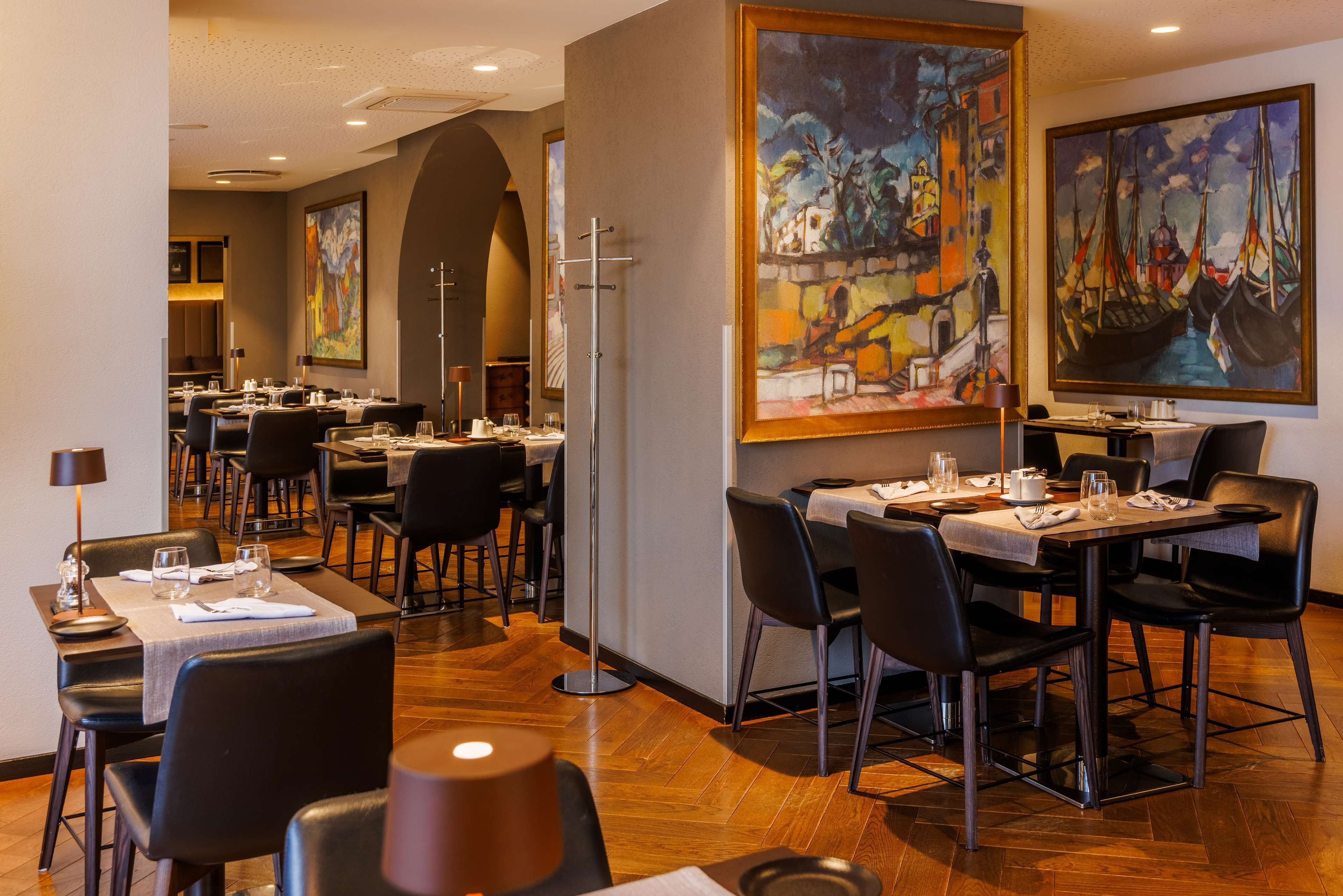 Un restaurante con varias mesas, sillas negras y cuadros en las paredes.