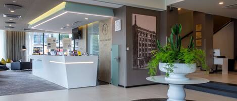 A modern hotel lobby with a reception desk, a large cactus plant, and a staircase.