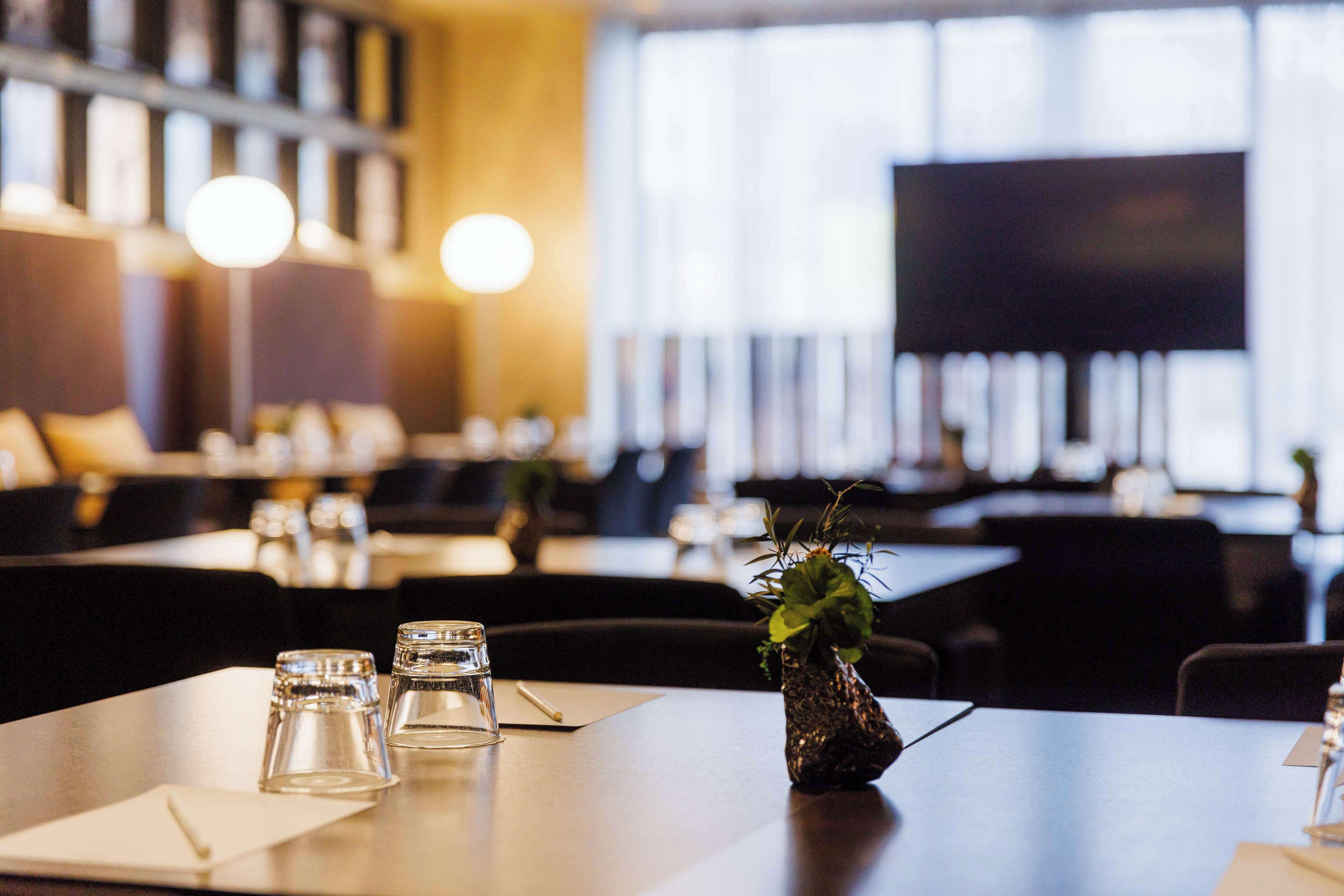 A restaurant with tables set for dining, a television screen, and a plant on the table.
