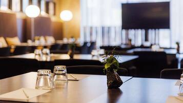 A restaurant with tables set for dining, a television screen, and a plant on the table.