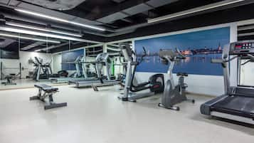 Een fitnessruimte met diverse trainingsapparaten, waaronder loopbanden en hometrainers, en een groot muurdecoratie van een stadsgezicht.